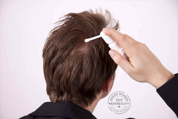 Applying topical hair treatment to the crown of the scalp with a spray applicator.