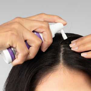 Woman applying FOLIGAIN TRIOXIDIL topical treatment along the part in her hair